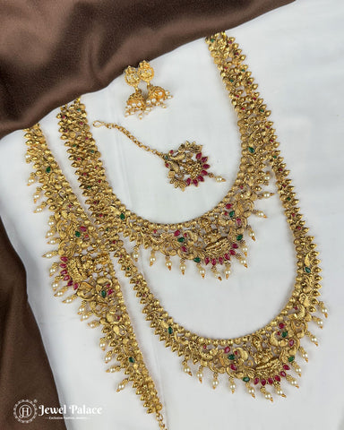 Gold necklace with red and green gemstones on a white and brown fabric background, brand 'Jewel Palace' visible.