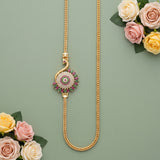 A gold chain necklace with a decorative circular pendant featuring pink and green stones, styled with pink and yellow roses on a sage green background.