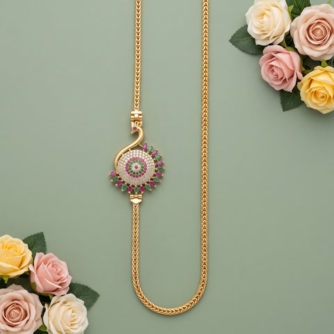 A gold chain necklace with a decorative circular pendant featuring pink and green stones, styled with pink and yellow roses on a sage green background.
