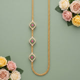 A gold chain necklace with three ornate diamond-shaped pendants, each decorated with small white stones and a central pink and green floral motif, arranged on a muted green background with decorative roses in the corners.