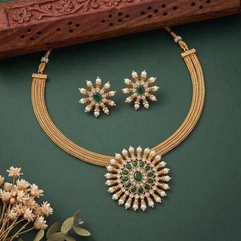 Gold-tone Indian Kundan jewelry set featuring a multi-strand necklace with a large circular pendant, matching stud earrings, and decorative dried flowers on a dark green background.