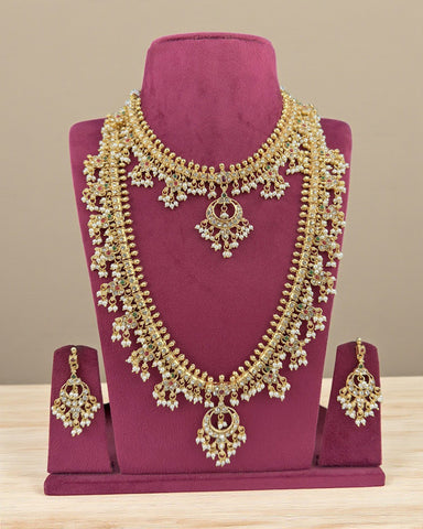 Gold necklace and earrings set on a purple stand with a beige background