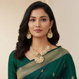 Woman wearing a green saree with gold border and pearl jewelry on a beige background