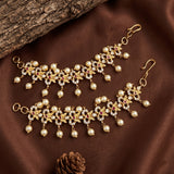 Gold-toned traditional Indian jhumka earrings with white faux pearls, clear rhinestones, and small red floral accents, arranged on a brown satin fabric with a log prop.