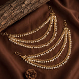 Gold-toned multi-strand chain jewelry with small white pearl-like beads, arranged on brown satin fabric with a piece of wood and a small pinecone prop.