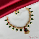 Gold necklace with green and red stones on a white surface with a red fabric background, branded 'Jewel Palace'.