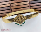 Gold belt with decorative clasp and green beads on a white surface with wooden background