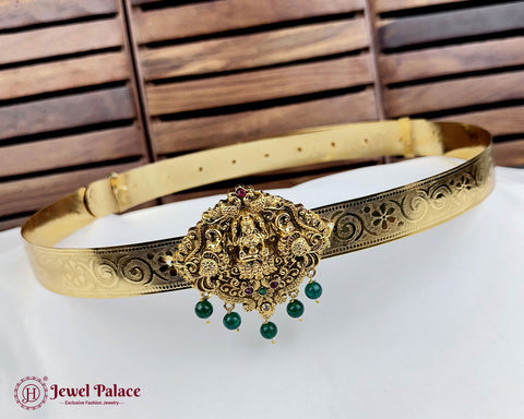 Gold belt with decorative clasp and green beads on a white surface with wooden background