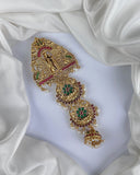 Gold jewelry piece with red and green gemstones on a white fabric background