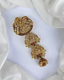 Gold jewelry piece with red and green gemstones on a white fabric background