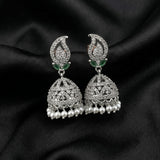 A pair of silver-toned Indian jhumka earrings adorned with clear crystals, small green stone accents, and dangling pearl-like beads, displayed on a black satin fabric background.