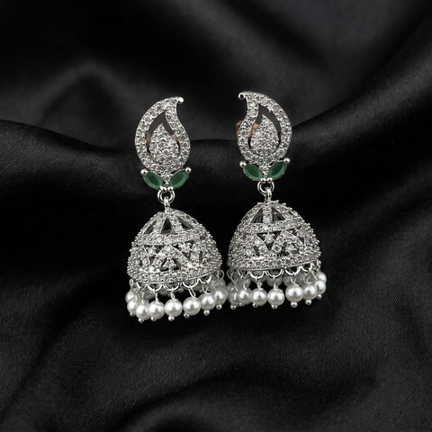 A pair of silver-toned Indian jhumka earrings adorned with clear crystals, small green stone accents, and dangling pearl-like beads, displayed on a black satin fabric background.