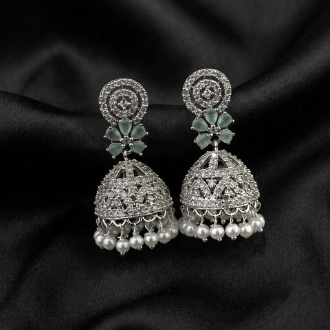 A pair of silver-toned Indian jhumka earrings with green stone floral accents and dangling pearl-like beads, displayed on a black satin fabric background.