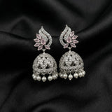 A pair of silver-toned Indian jhumka earrings with pink gemstone floral accents and dangling white pearls, displayed on a draped black satin fabric.