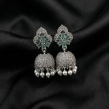 A pair of silver-toned Indian jhumka earrings with green enamel floral tops, pavé-set stones, and dangling pearl beads, displayed on a black satin fabric background.
