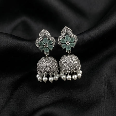 A pair of silver-toned Indian jhumka earrings with green enamel floral tops, pavé-set stones, and dangling pearl beads, displayed on a black satin fabric background.