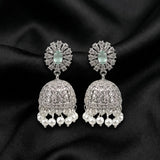 A pair of silver-toned Indian jhumka earrings with clear pavé stones and dangling white pearls, displayed on a black satin fabric background.