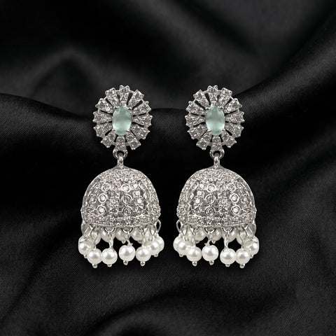 A pair of silver-toned Indian jhumka earrings with clear pavé stones and dangling white pearls, displayed on a black satin fabric background.