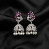 A pair of silver-toned Indian jhumka earrings decorated with pink gemstones at the top, pavé-set clear stones in the middle, and dangling white pearls at the bottom, displayed on a black satin fabric background.