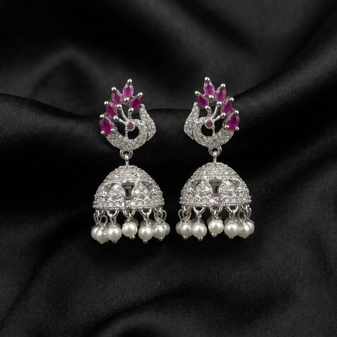 A pair of silver-toned Indian jhumka earrings decorated with pink gemstones at the top, pavé-set clear stones in the middle, and dangling white pearls at the bottom, displayed on a black satin fabric background.