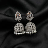 A pair of silver-toned Indian jhumka earrings with rectangular clear crystals and dangling white faux pearls, displayed on a black satin fabric background.