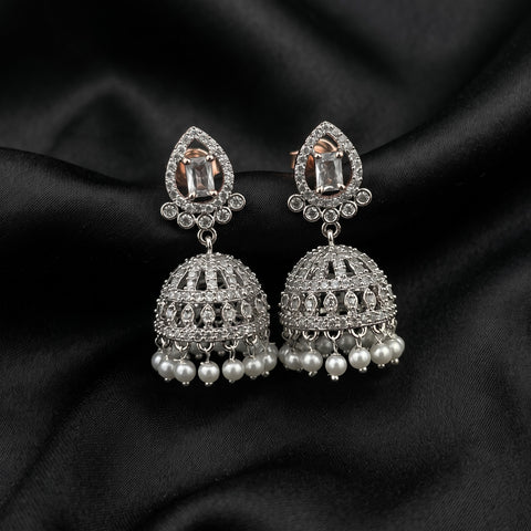 A pair of silver-toned Indian jhumka earrings with rectangular clear crystals and dangling white faux pearls, displayed on a black satin fabric background.