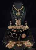 A gold and green traditional Indian jewelry set displayed on a black mannequin bust and stand, including a necklace, earrings, bracelet, and multiple matching jewelry pieces, with a matching necklace laid out in front on a dark marble surface.