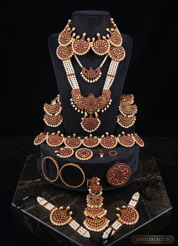 A traditional Indian jewelry set displayed on a black velvet jewelry bust and base. The set includes a statement necklace, a matching chain necklace, a large pendant, earrings, a bracelet, and a wristlet, all decorated with gold, brown, and white elements.
