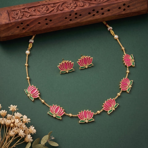 Gold-tone lotus flower jewelry set featuring a necklace and matching earrings, decorated with pink and green enamel lotus motifs and small pearl-like beads, displayed on a dark green background with decorative dried flowers and a carved wooden prop.