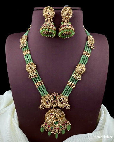 Green beaded necklace with gold accents and matching earrings on a purple stand.