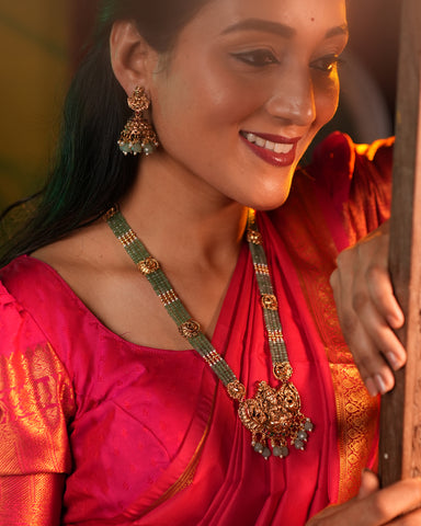 Woman wearing traditional jewelry, including a necklace and earrings, with a blurred background.