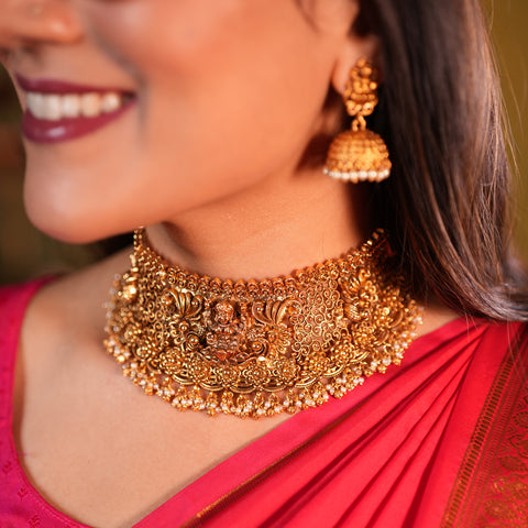 Woman wearing a gold necklace and earrings with a blurred background