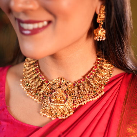 Woman wearing a gold necklace and earrings with a red saree