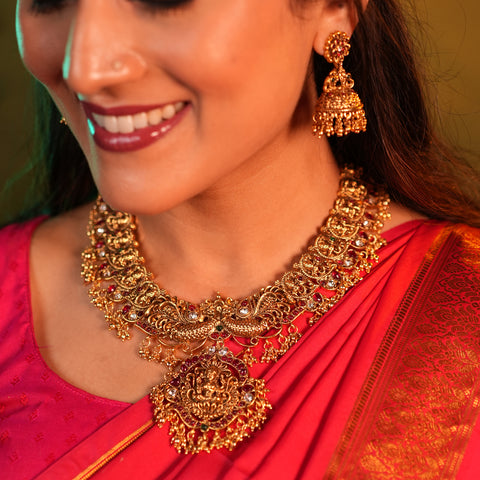 Woman wearing gold jewelry including a necklace and earrings, with a red saree.