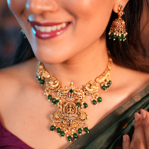 Woman wearing a gold necklace with green beads and matching earrings.