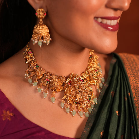 Close-up of a woman wearing gold jewelry with green beads, including a necklace and earrings.