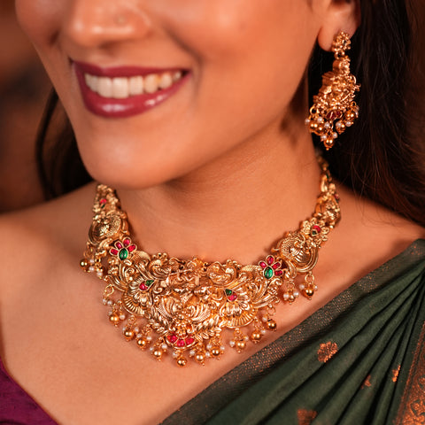 Close-up of a woman wearing a gold necklace and earrings with a blurred background