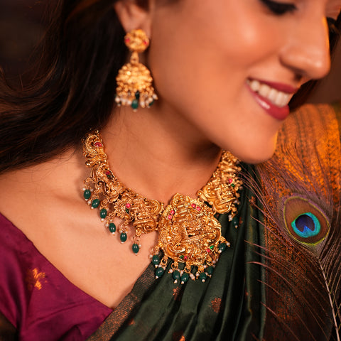 Woman wearing gold jewelry with a peacock feather, close-up of necklaces and earrings.