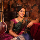Woman in traditional attire with jewelry, sitting in a decorative setting.