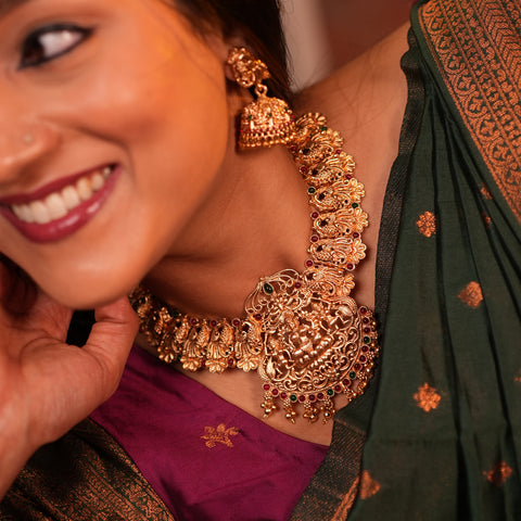 Woman wearing a gold necklace and earrings with a green saree.