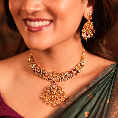 Woman wearing a gold necklace and earrings with a blurred background