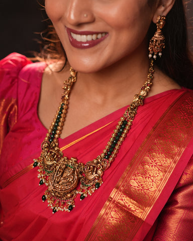 Woman wearing a red saree with gold jewelry, including a necklace and earrings.