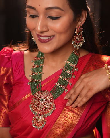 Woman wearing a red saree with gold border and elaborate green and red jewelry set.