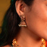 Close-up of a person wearing a gold earring with green gemstones.