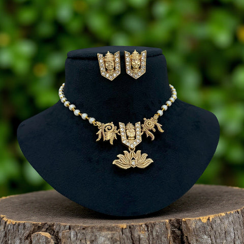 Gold necklace and earrings on a black velvet stand with a green blurred background