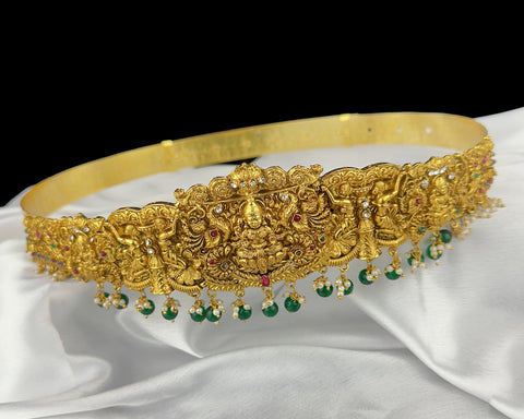 Gold headband with intricate designs and green gemstones on a white fabric background