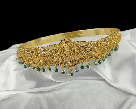 Gold necklace with green and red gemstones on a white fabric background