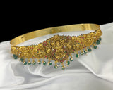 Gold headband with green and red stones on a white fabric background