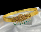Gold headband with green and red gemstones on a white fabric background