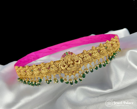 Gold necklace with green stones on a pink fabric background